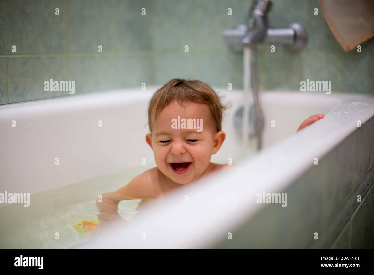 oncept de la felicidad familiar y de la paternidad. Lindo bebé caucásico tomando un baño en casa, riendo con los ojos cerrados. Salpicaduras de agua, en el Foto de stock