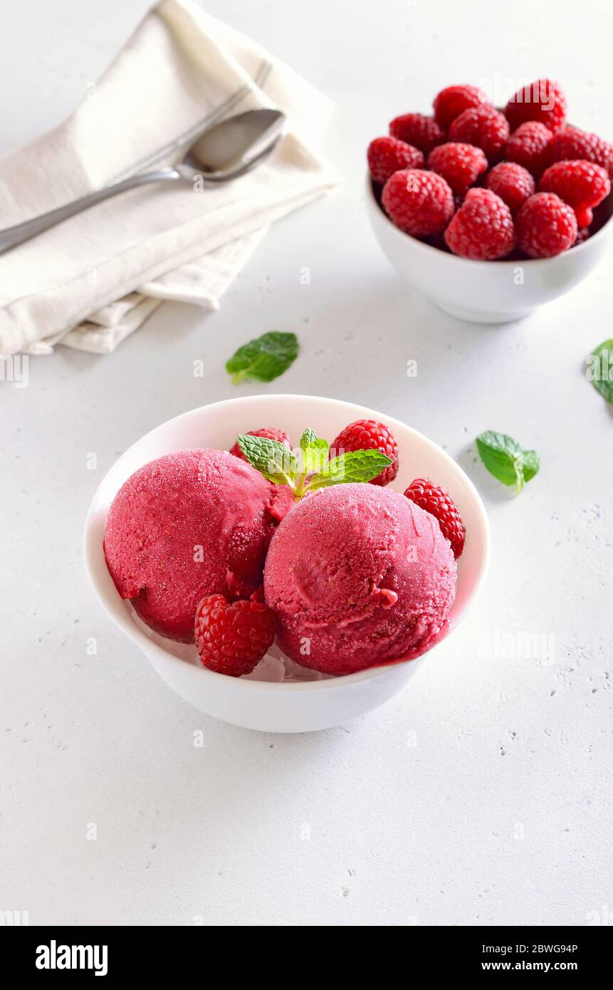 Frambuesa bola de helado con frambuesas frescas en un tazón blanco. Postre frío de verano Foto de stock