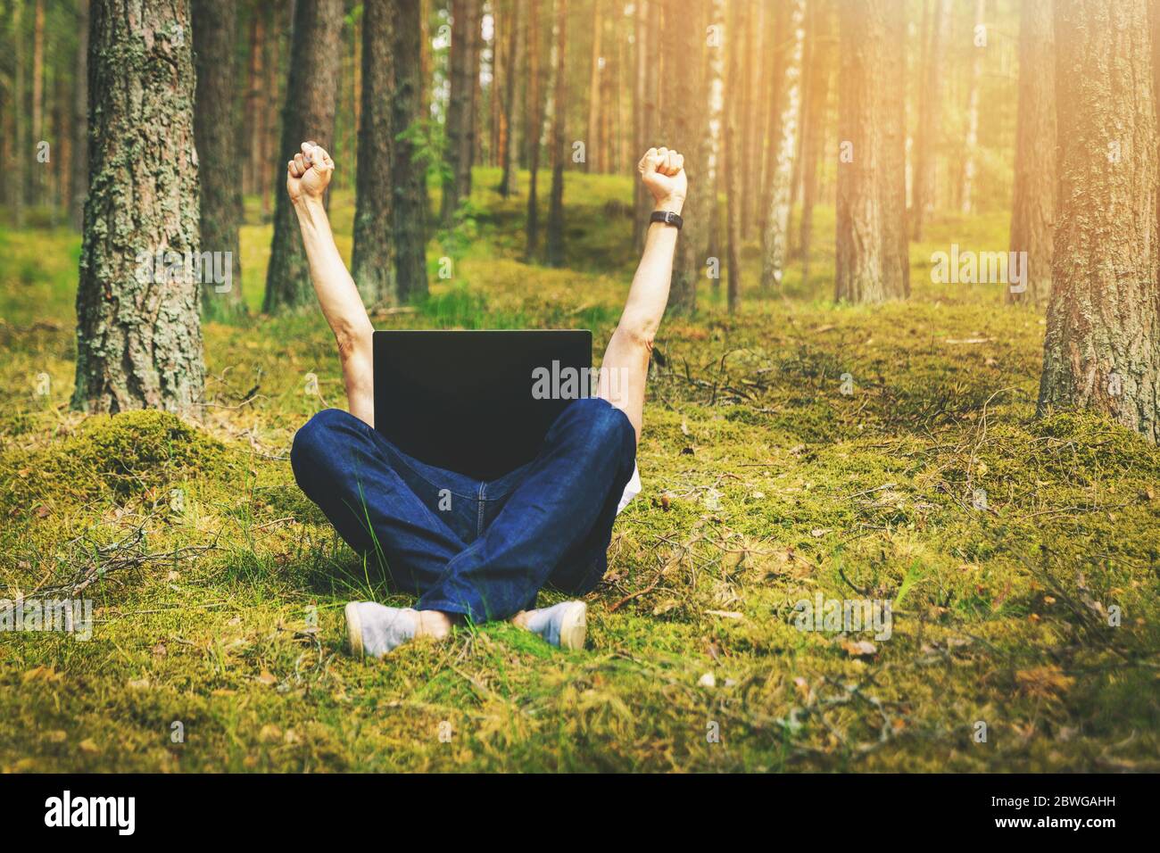 teletrabajo - hombre con portátil tumbado en el musgo en el bosque con las manos levantadas Foto de stock