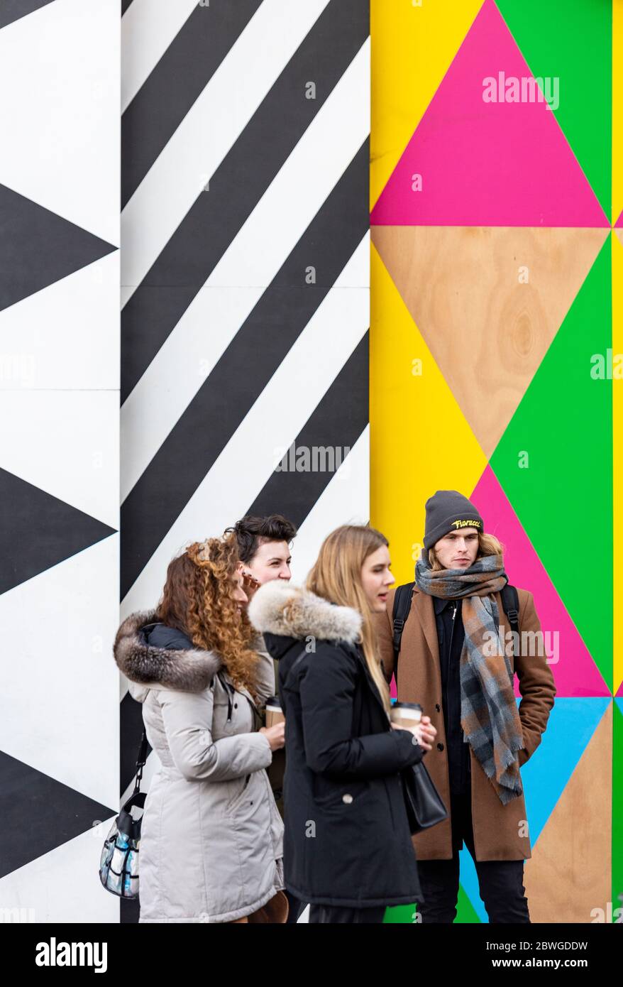 Un grupo de adolescentes de moda que se encuentran en Grosvenor Arch Entrada a la central eléctrica de Battersea reurbanización frente a un obra de arte colorido Foto de stock