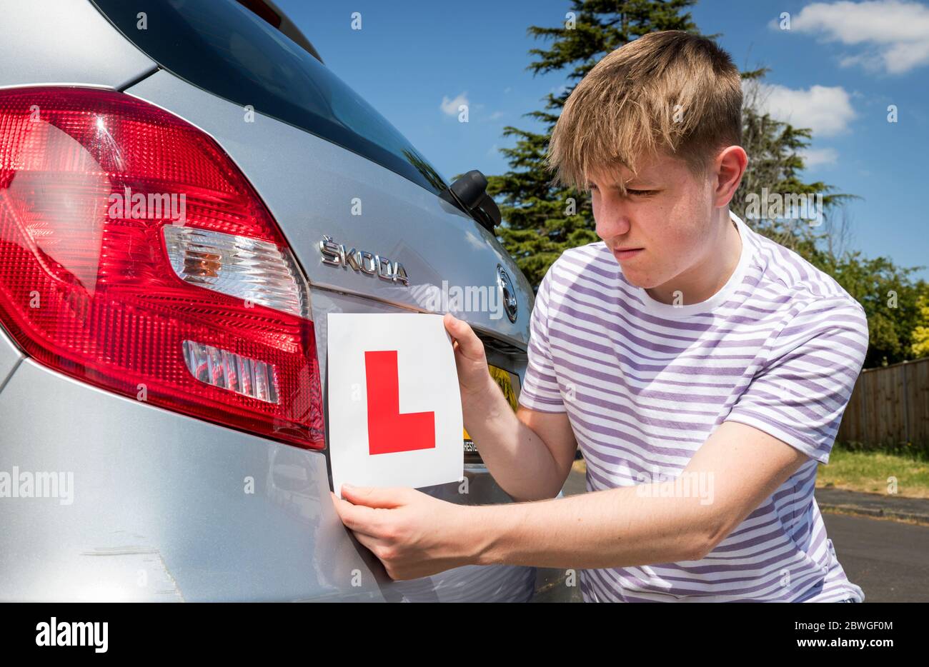 Conductor adolescente que aprende añadiendo placas L al coche de sus padres listo para una lección. Foto de stock