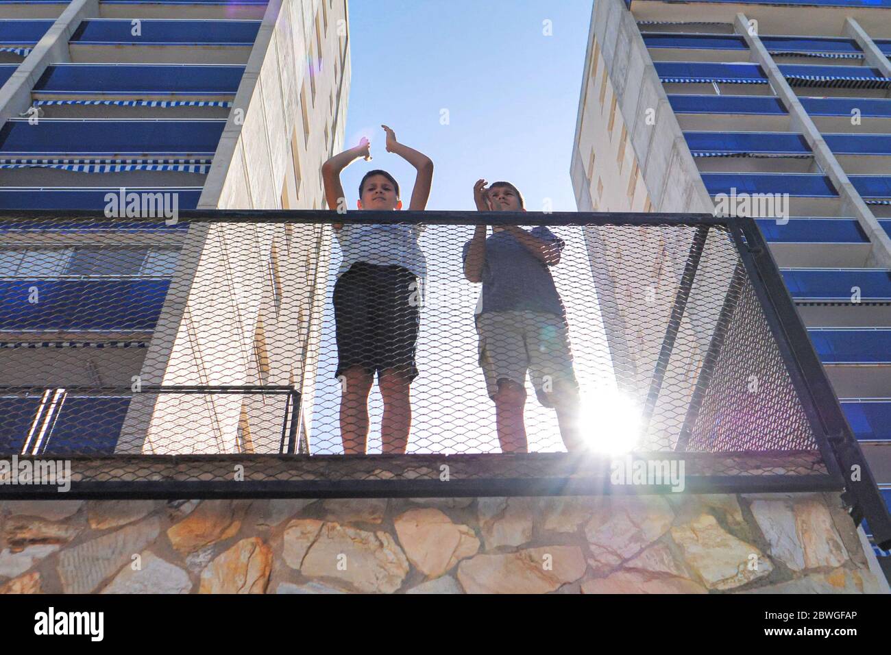 Los niños se palman, aplaudiendo desde el balcón de la terraza para apoyar a los médicos, enfermeras, trabajadores del hospital durante la cuarentena pandémica del Coronavirus Covid-19 Foto de stock
