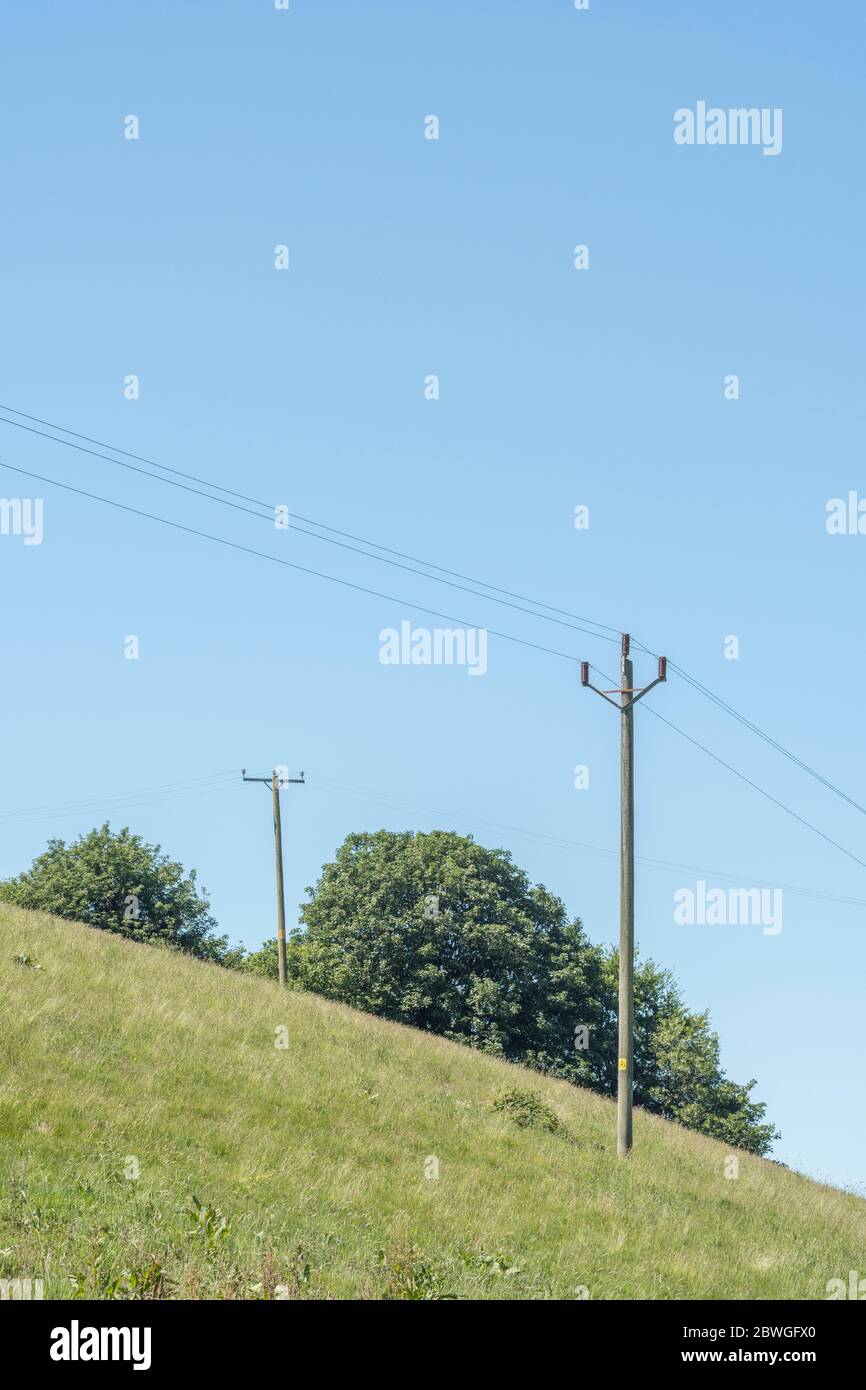 Polo de distribución de electricidad doméstica en un campo de heno de verano, con cielo azul y nubes esponjosas. Concepto de electricidad para el hogar rural. Foto de stock