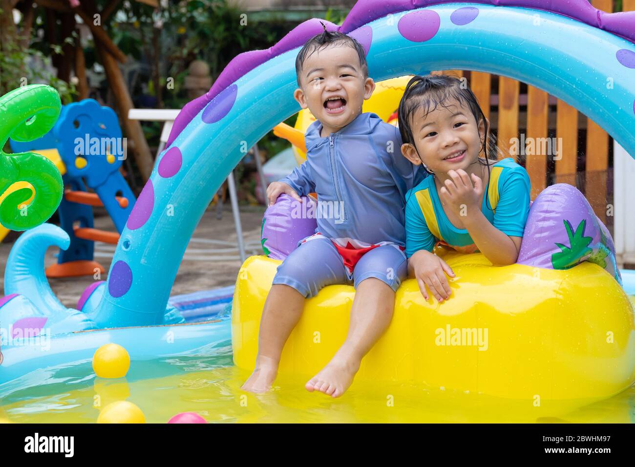 Niños asiáticos jugando en la piscina inflable para bebés. Los niños nadan y zambullen en el colorido centro de juegos del jardín. Chica feliz jugando con juguetes de agua caliente Fotografía