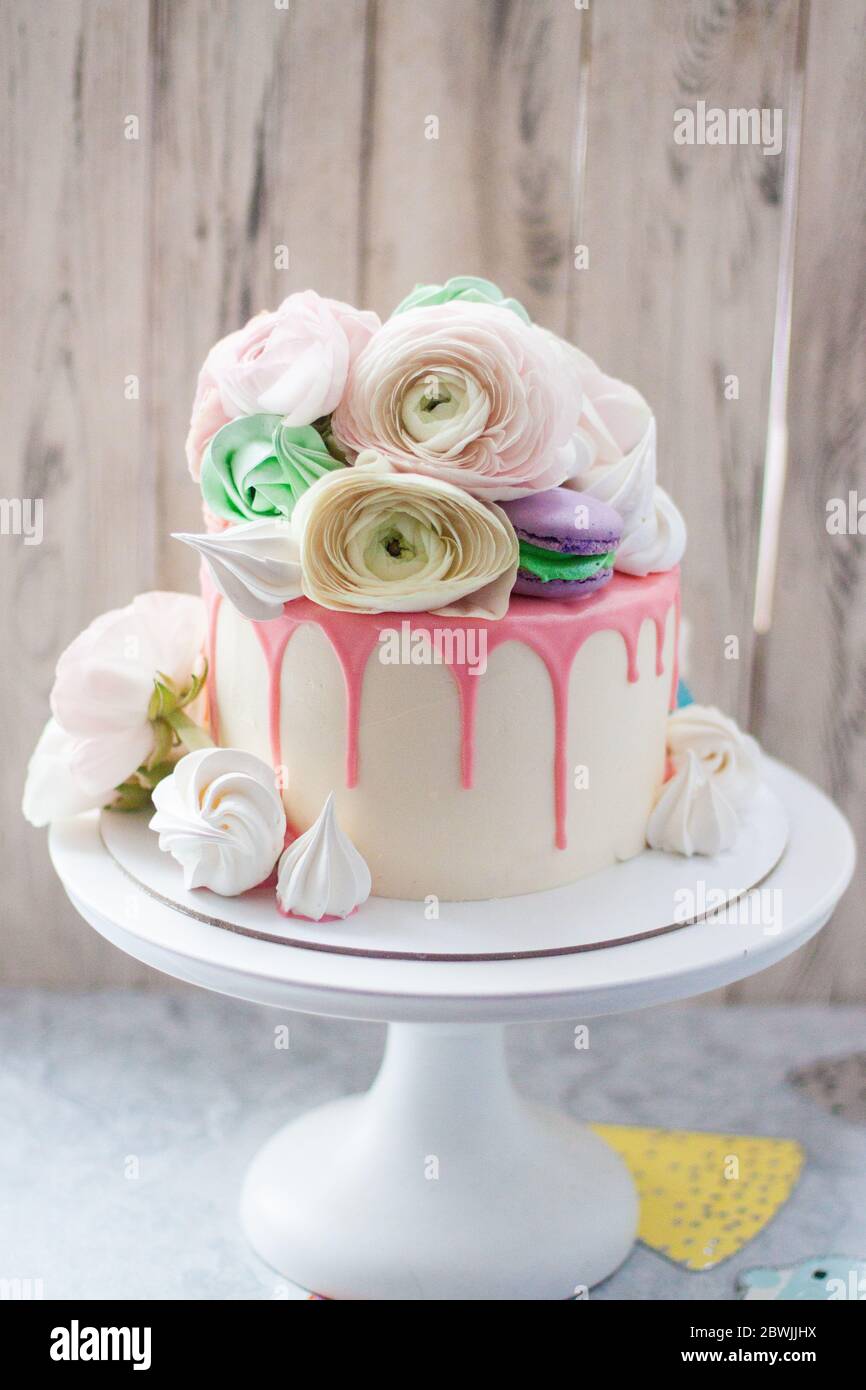 Pastel blanco con chocolate rosa derretido, merengues, macarrones y flores  frescas. Fondo rústico Fotografía de stock - Alamy