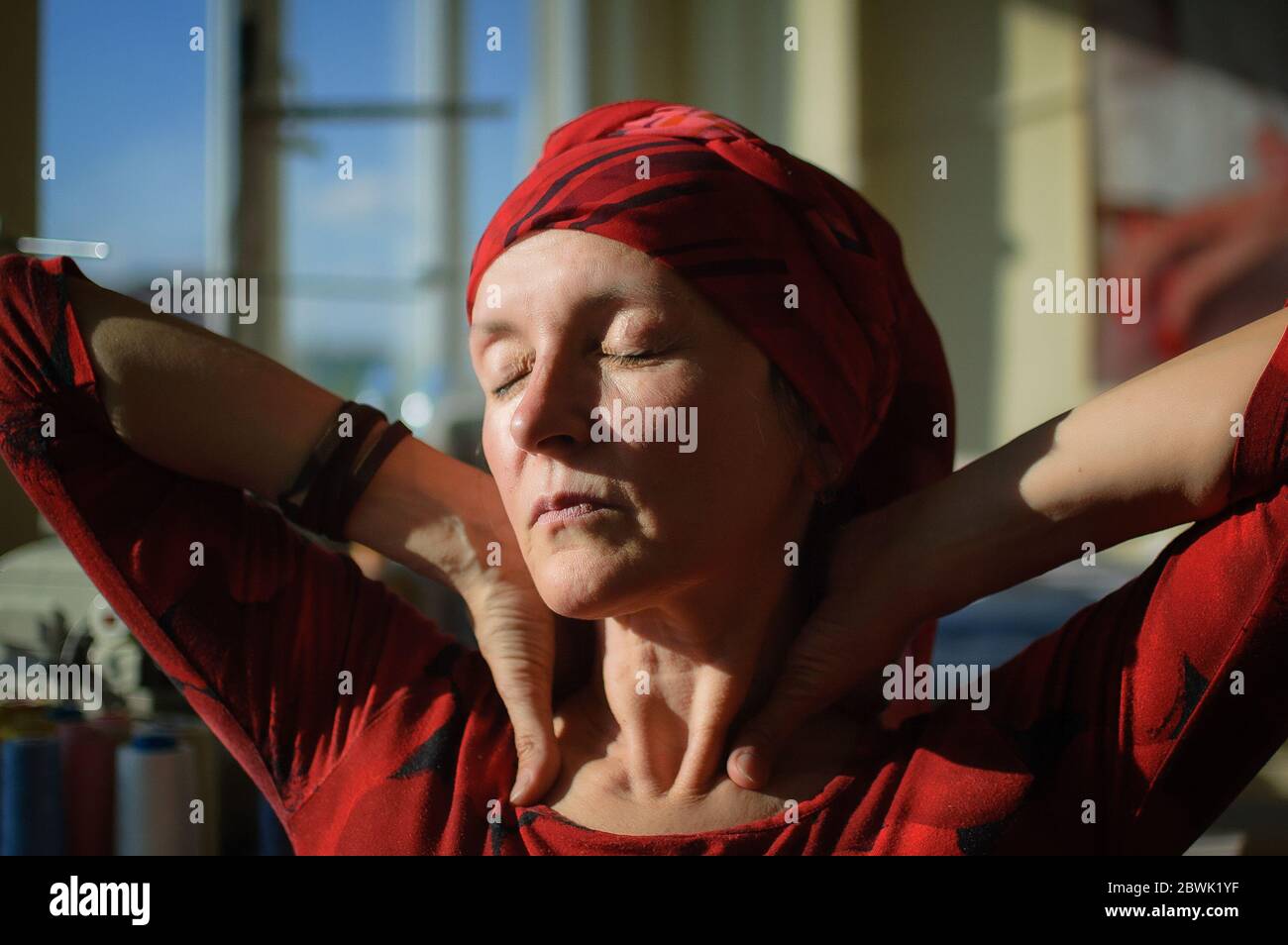 Retrato femenino de mujer madura vestida de ropa roja y sentada al final de su jornada de trabajo en la máquina de coser y el fondo de algodón bobbins Foto de stock