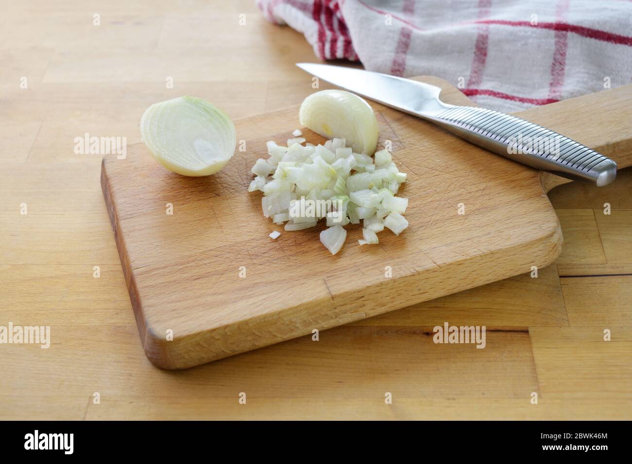 Cortar cebollas en pequeños cubos con un cuchillo de cocina en una tabla de cortar de madera, enfoque seleccionado, profundidad de campo estrecha Foto de stock