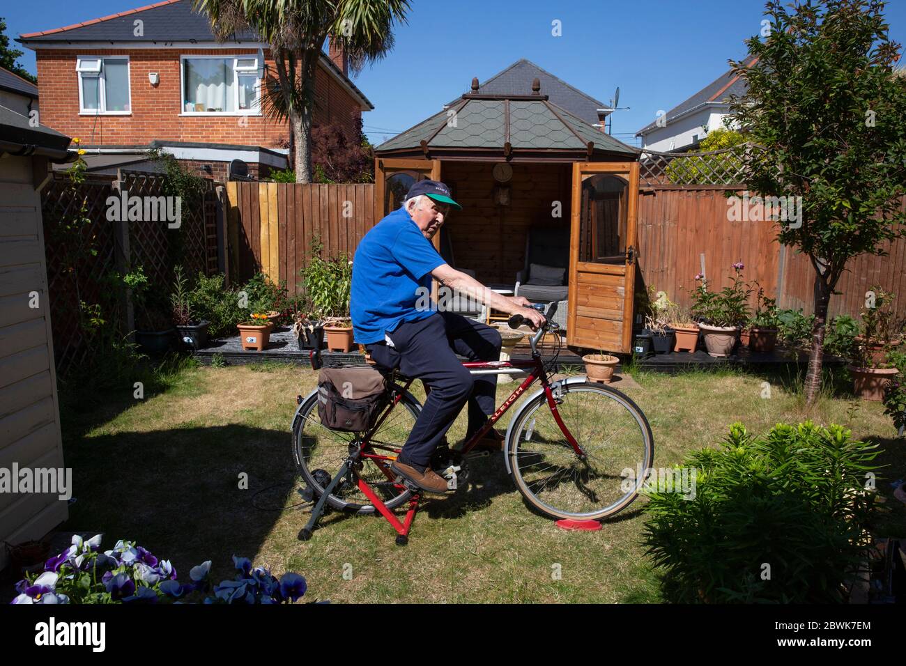 Pareja de ancianos, ambos en sus 80's mantenerse en forma en un entrenador de bicicleta se encuentra en su jardín trasero durante el cierre coronavirus, Southwest England, Reino Unido Foto de stock
