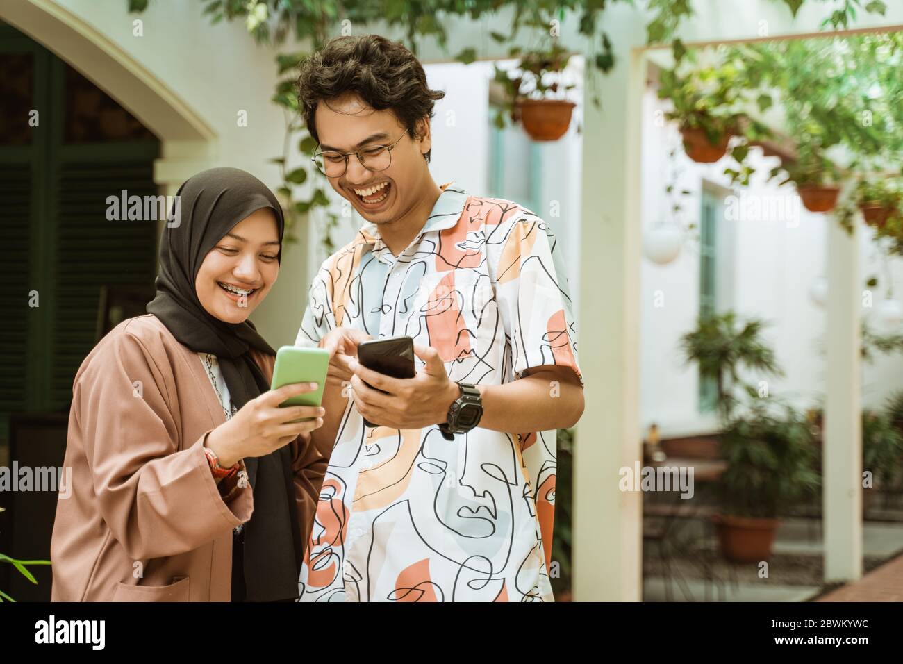 la joven pareja rió mientras sostenía un celular mientras estaba de pie mientras caminaba Foto de stock