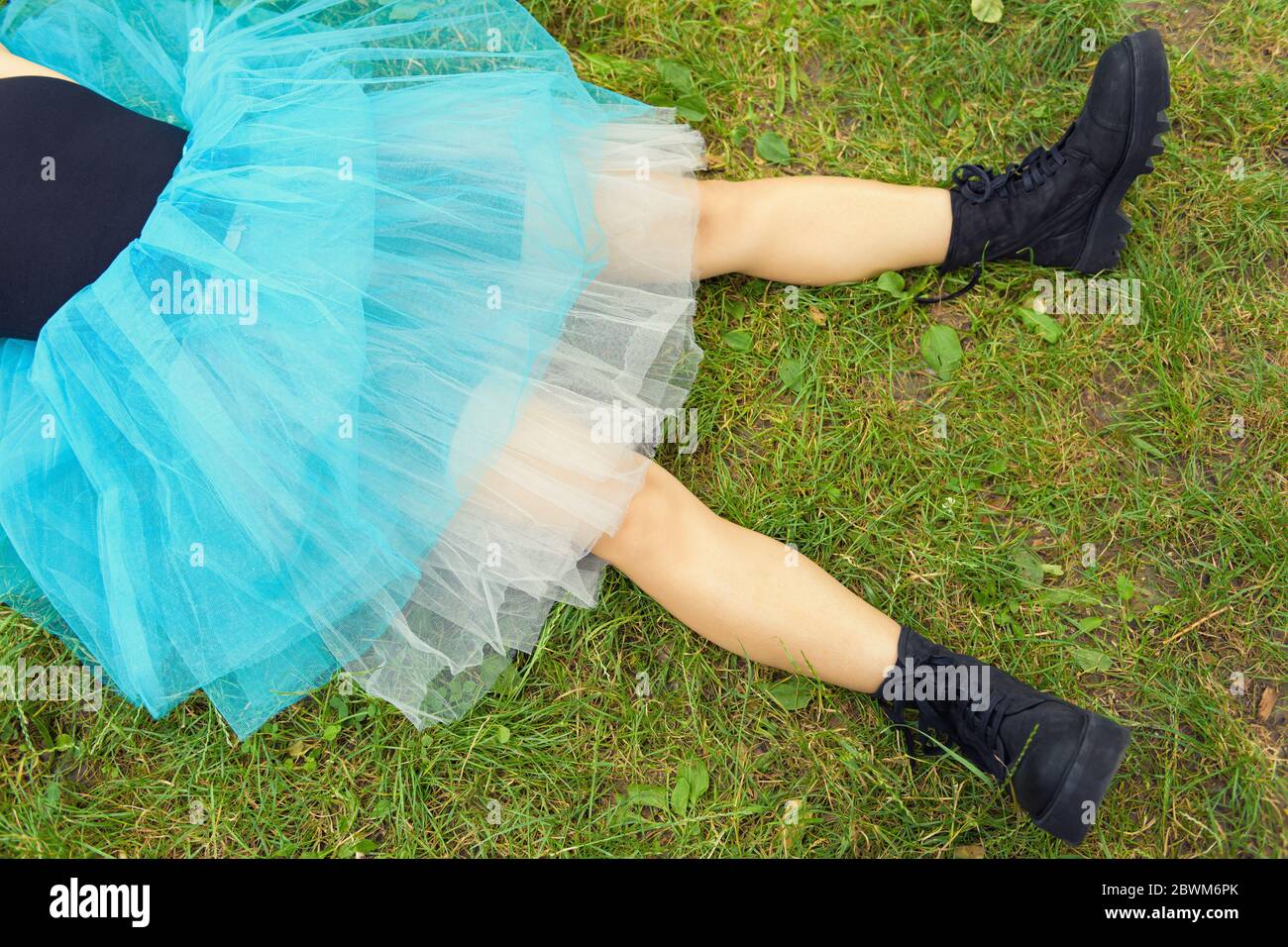 Mujer en grandes botas negras y una falda azul se encuentra en hierba  verde. Concepto después de la fiesta Fotografía de stock - Alamy