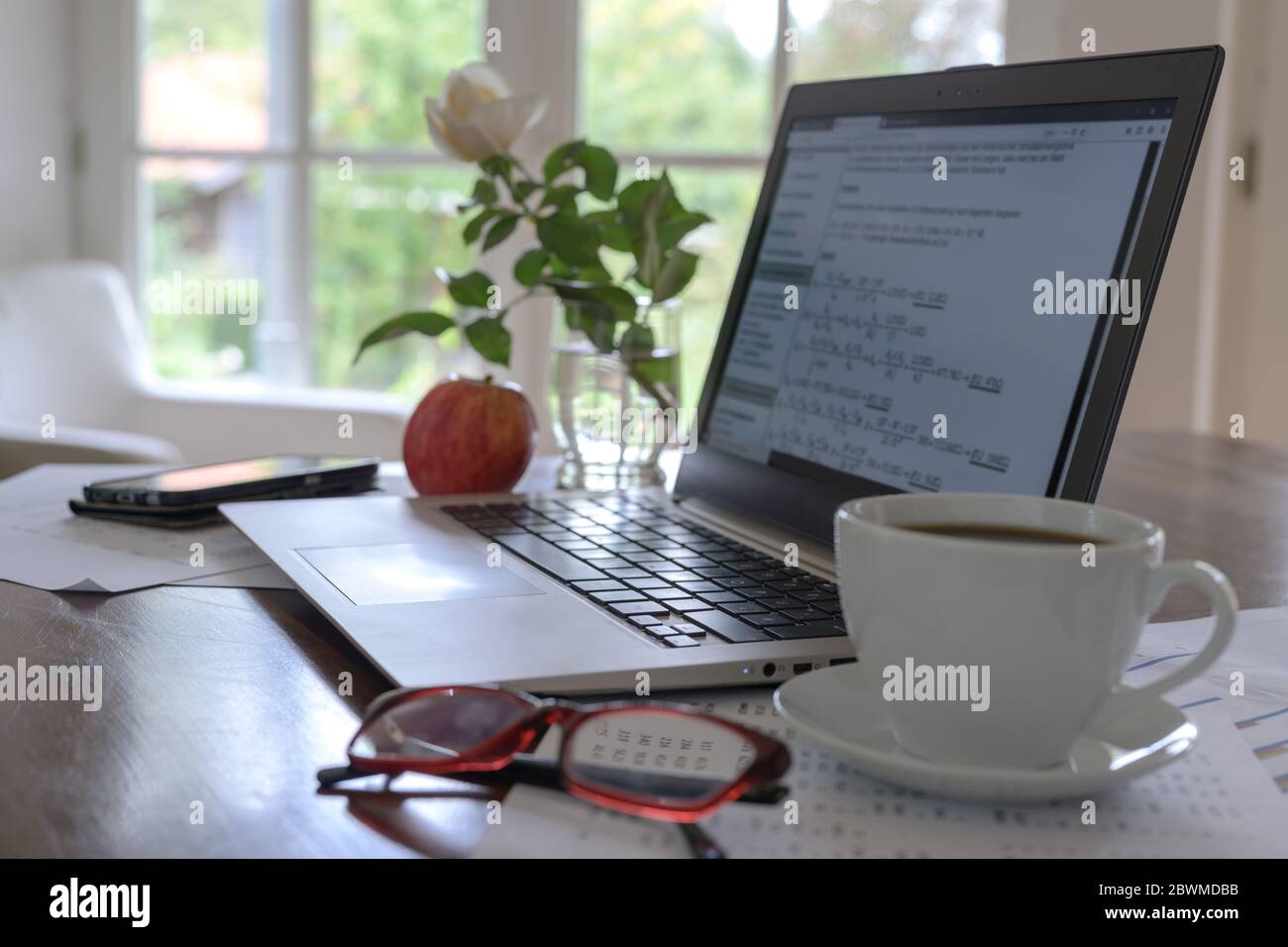 ordenador portátil con fórmulas matemáticas en la pantalla, taza de café, vasos y una manzana fresca en el escritorio de un estudiante, programador o un pequeño busi independiente Foto de stock