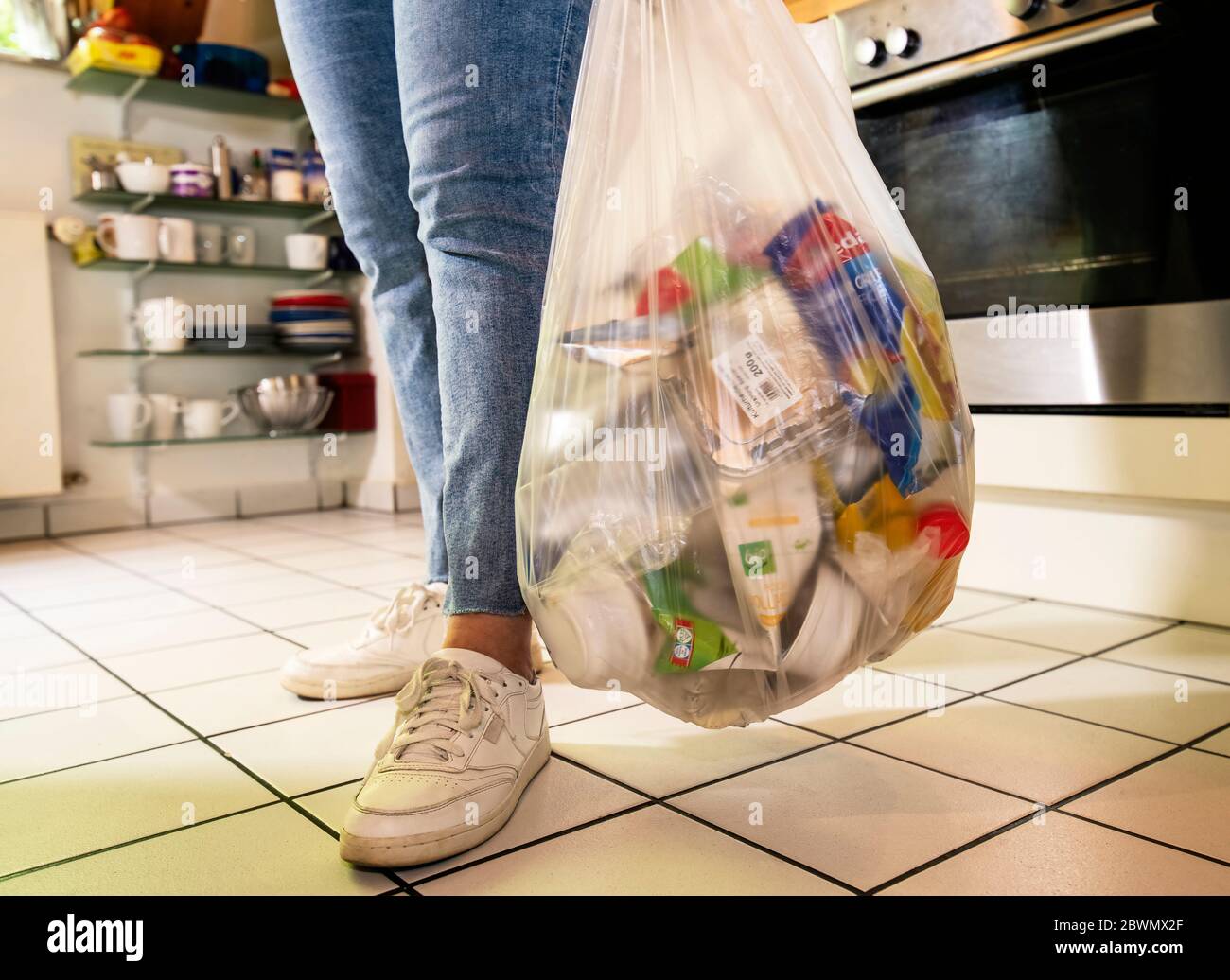 Mujer de pie en una cocina con una bolsa de plástico con residuos de plástico Foto de stock