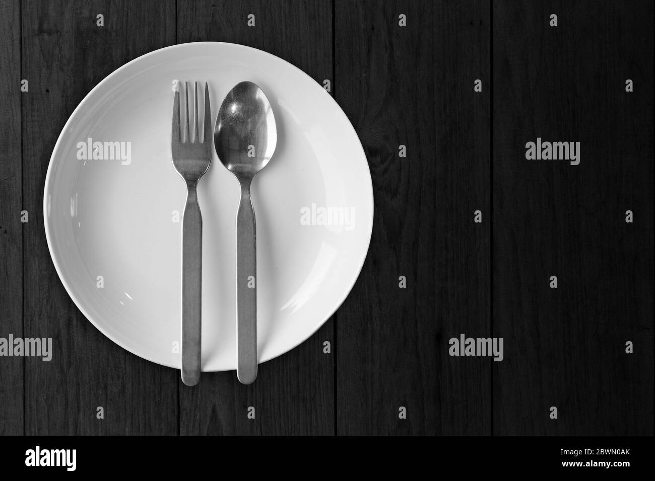 Plato blanco con cuchara de tenedor en blanco de madera negro vacío sin imagen de comida para la decoración. Foto de stock