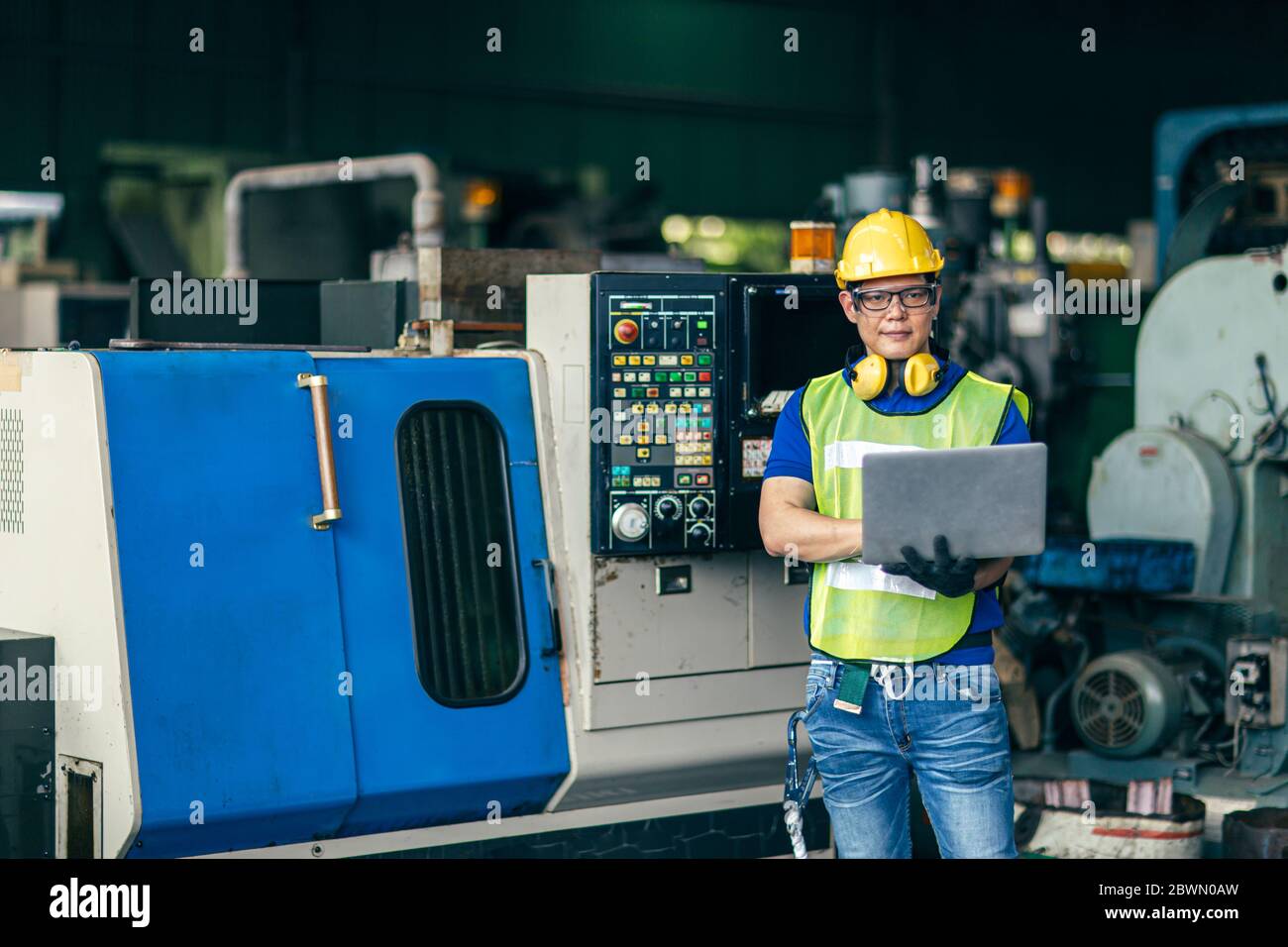 Ingeniero asiático trabajando programando la máquina en fábrica con ordenador portátil para configurar el proceso del programa, retrato mirando cámara de trabajador de la industria. Foto de stock