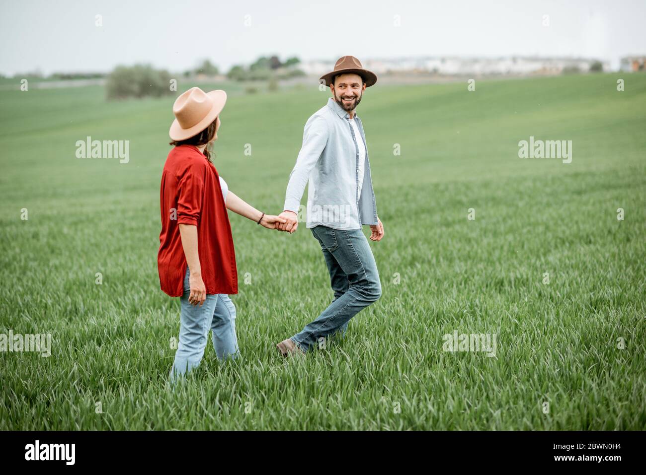 Mujer embarazada con su hombre divirtiéndose juntos, caminando por el campo verde. Feliz pareja esperando un bebé, joven concepto de familia Foto de stock