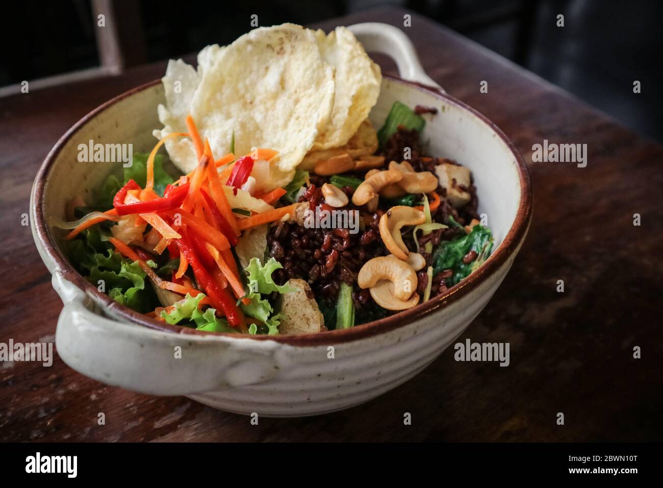 Arroz Rojo orgánico Nasi Goreng, arroz frito vegetariano con un montón de verduras, tofu y anacardos tostados en un tazón sobre fondo de madera Foto de stock