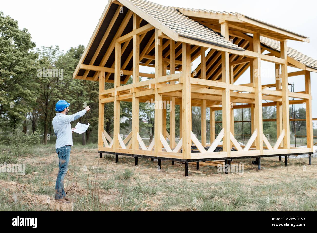 Arquitecto o constructor de pie con planos cerca de la estructura de la casa  de madera en el sitio de construcción al aire libre Fotografía de stock -  Alamy