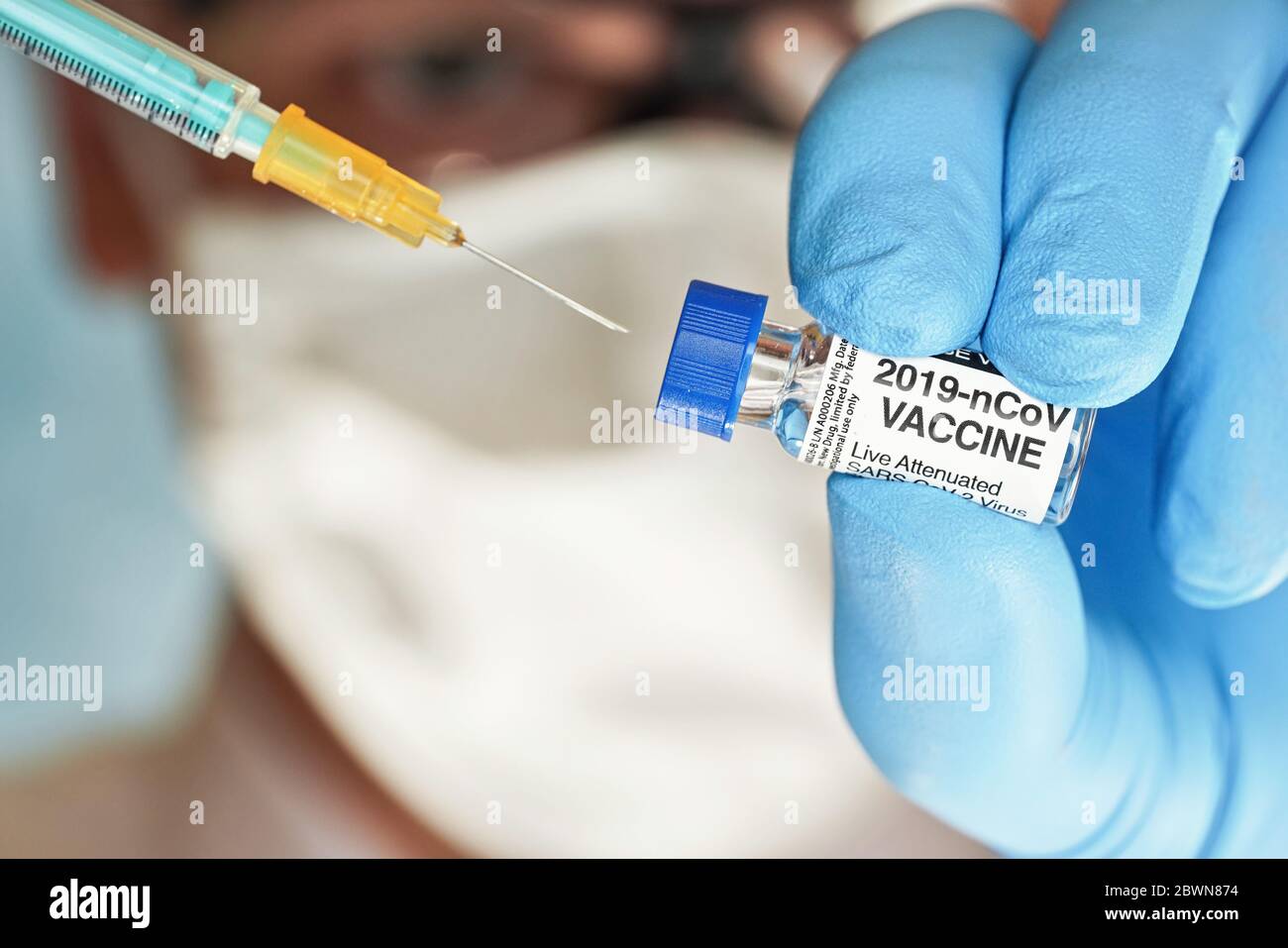 Hombre mano en guante azul de nitrilo mantener un pequeño vial con la vacuna contra el coronavirus, para inyectarlo con jeringa verde naranja, cara borrosa máscara blanca del virus en la espalda Foto de stock