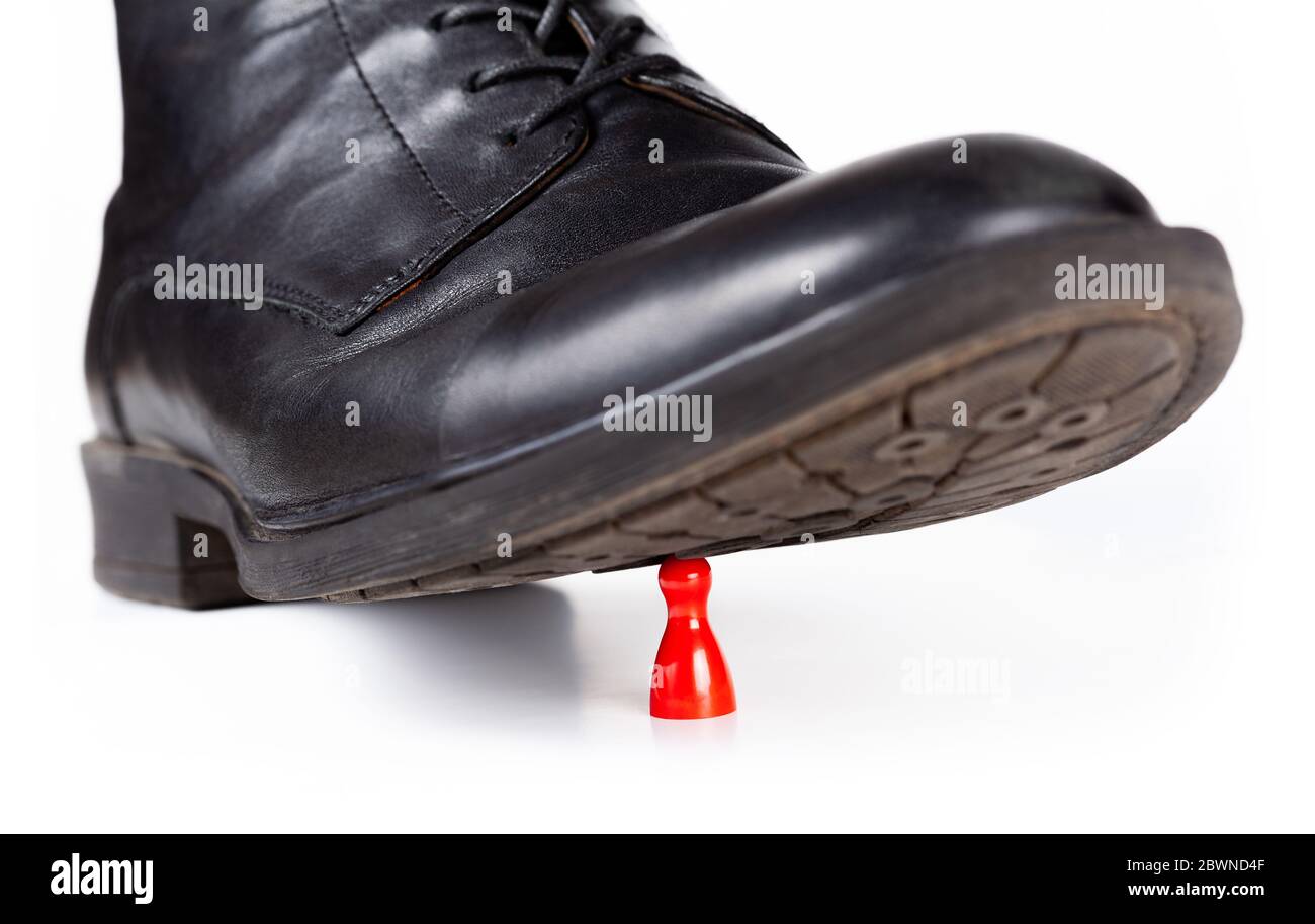 Bota de estilo negro y aplastar una pequeña pieza de juego de peón rojo bajo la suela. Grande vs pequeño, poder, peligro e impotencia concepto abstracto Foto de stock