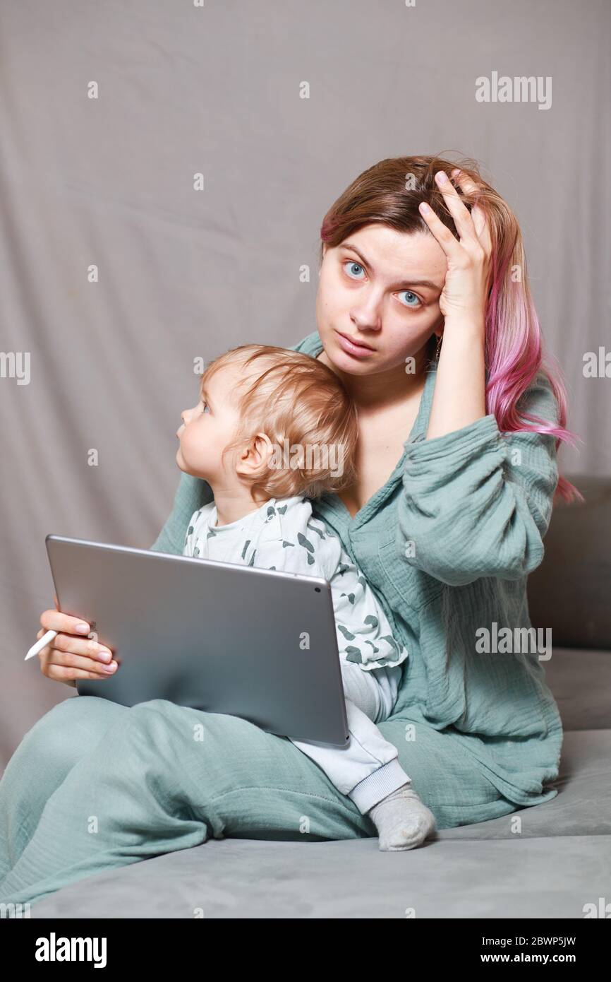 Quédese en casa, mamá trabaja remotamente en un ordenador portátil, cuidando a su hijo. Una joven madre en licencia de maternidad está tratando de trabajar como una mujer independiente Foto de stock