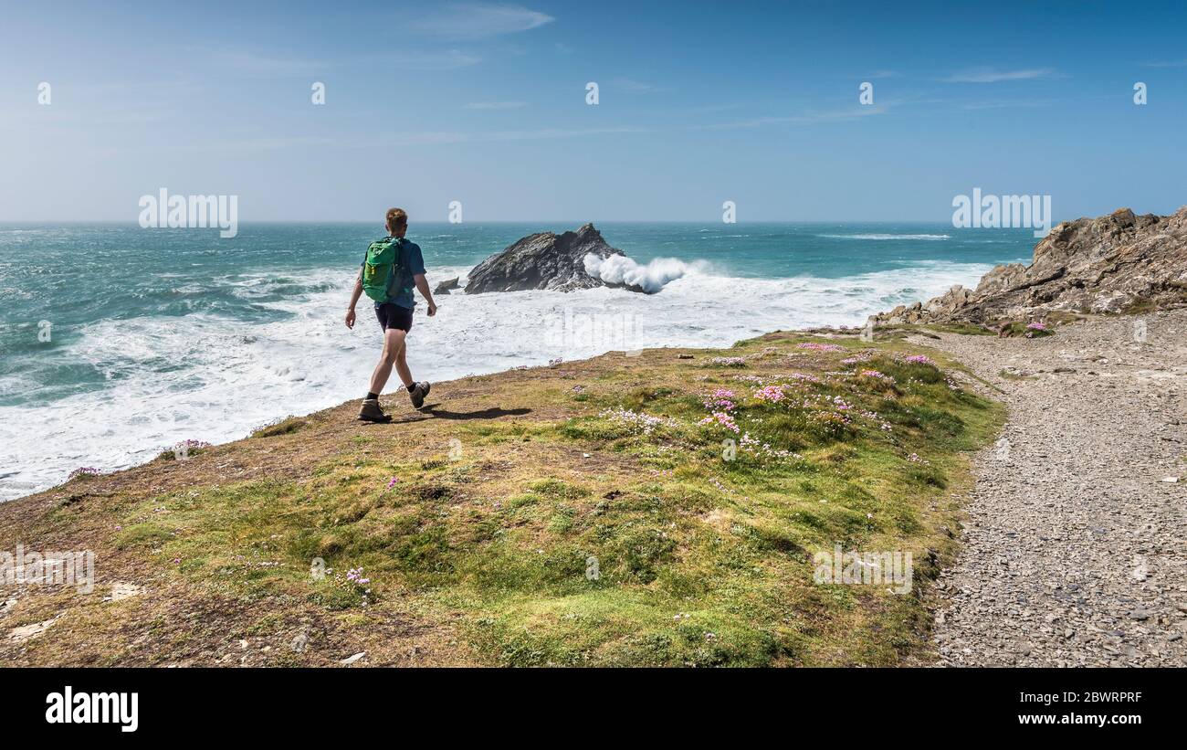 Una vista panorámica de un caminante observando olas salvajes rompiendo sobre Goose Island mientras camina por la costa de Penire Point East en Newquay en Cornwall. Foto de stock