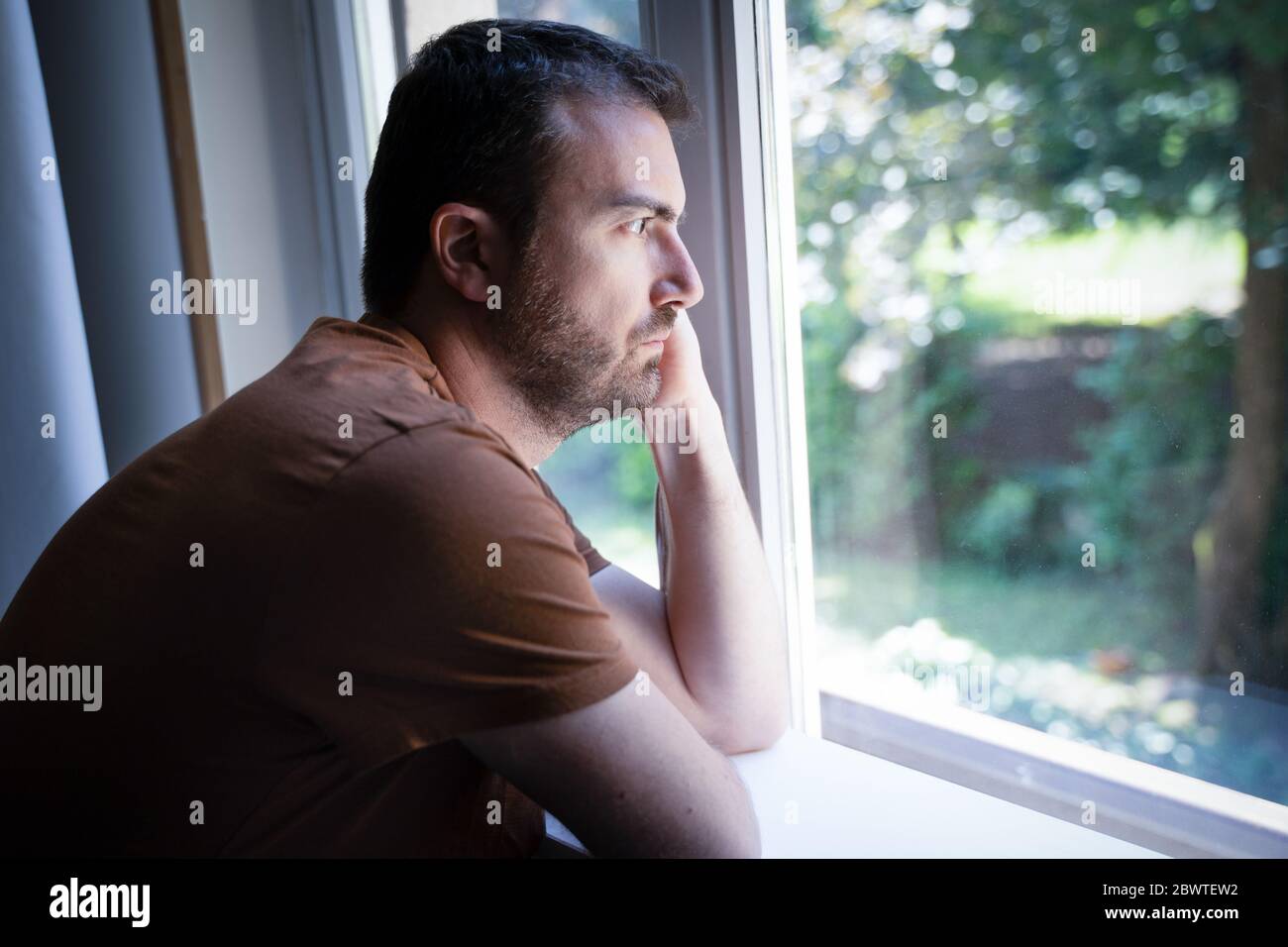 Retrato de un hombre que se siente triste y mirando a través de la ventana Foto de stock