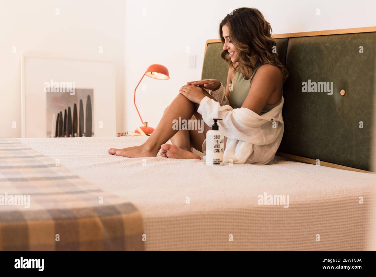 Mujer latina aplicando crema corporal de un recipiente blanco con espacio de copia para calificar Foto de stock
