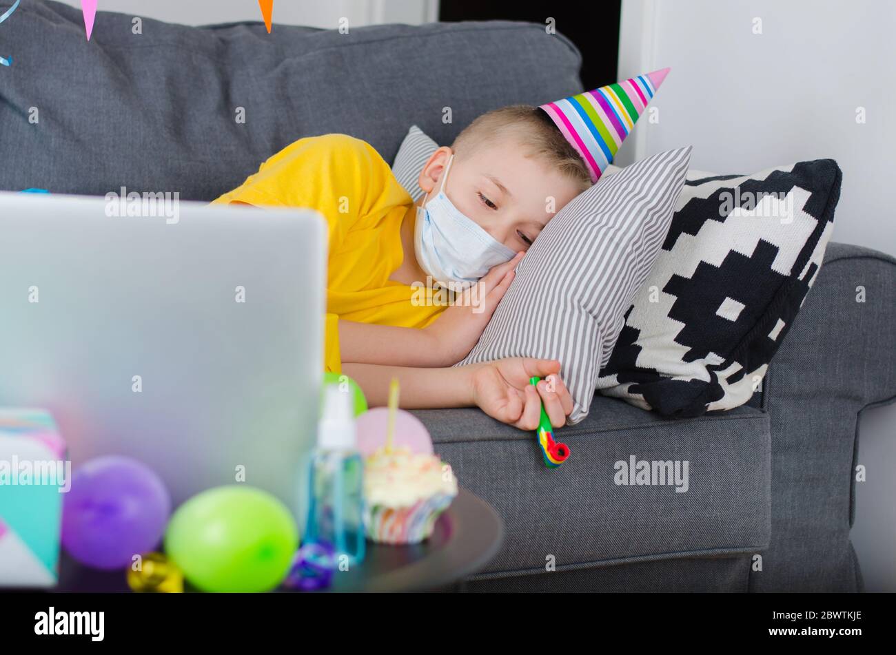 Nino Triste En La Mascara De La Medicina Y Casquillo Festivo Celebra Cumpleanos Por Llamada De Video A La Computadora Portatil Cuarentena Cumpleanos En Linea En Aislamiento Evento Virtual Mantener Fotografia De