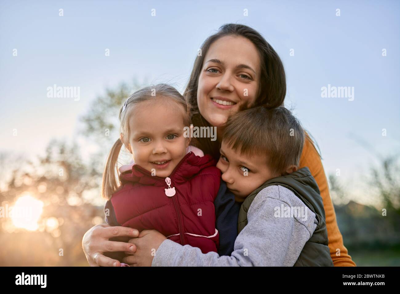 Retrato de madre feliz abrazando a dos niños al aire libre Foto de stock