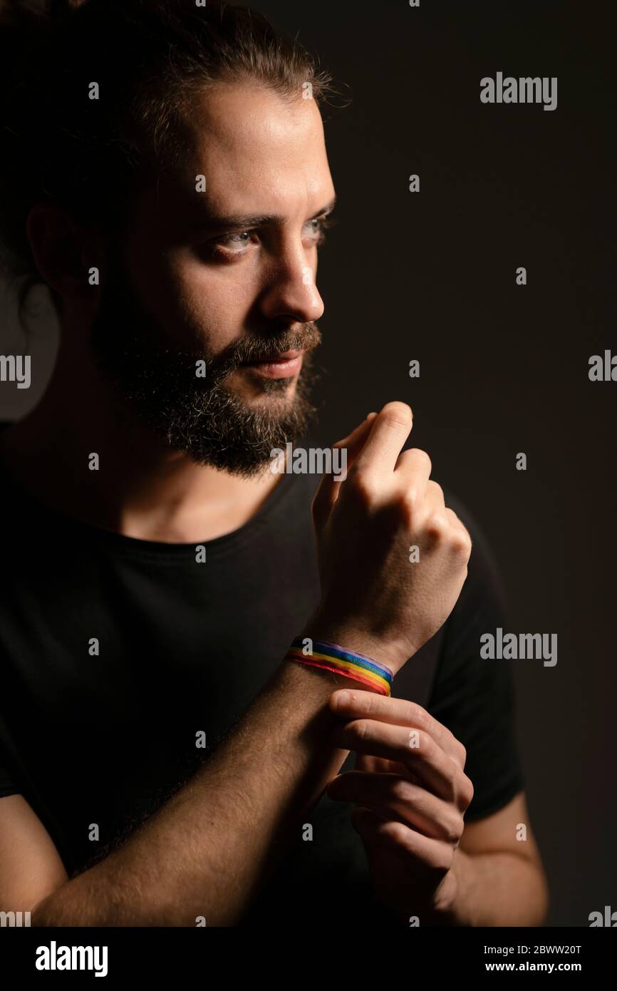 Retrato de un joven barbudo con pulsera arco iris sobre fondo oscuro Foto de stock