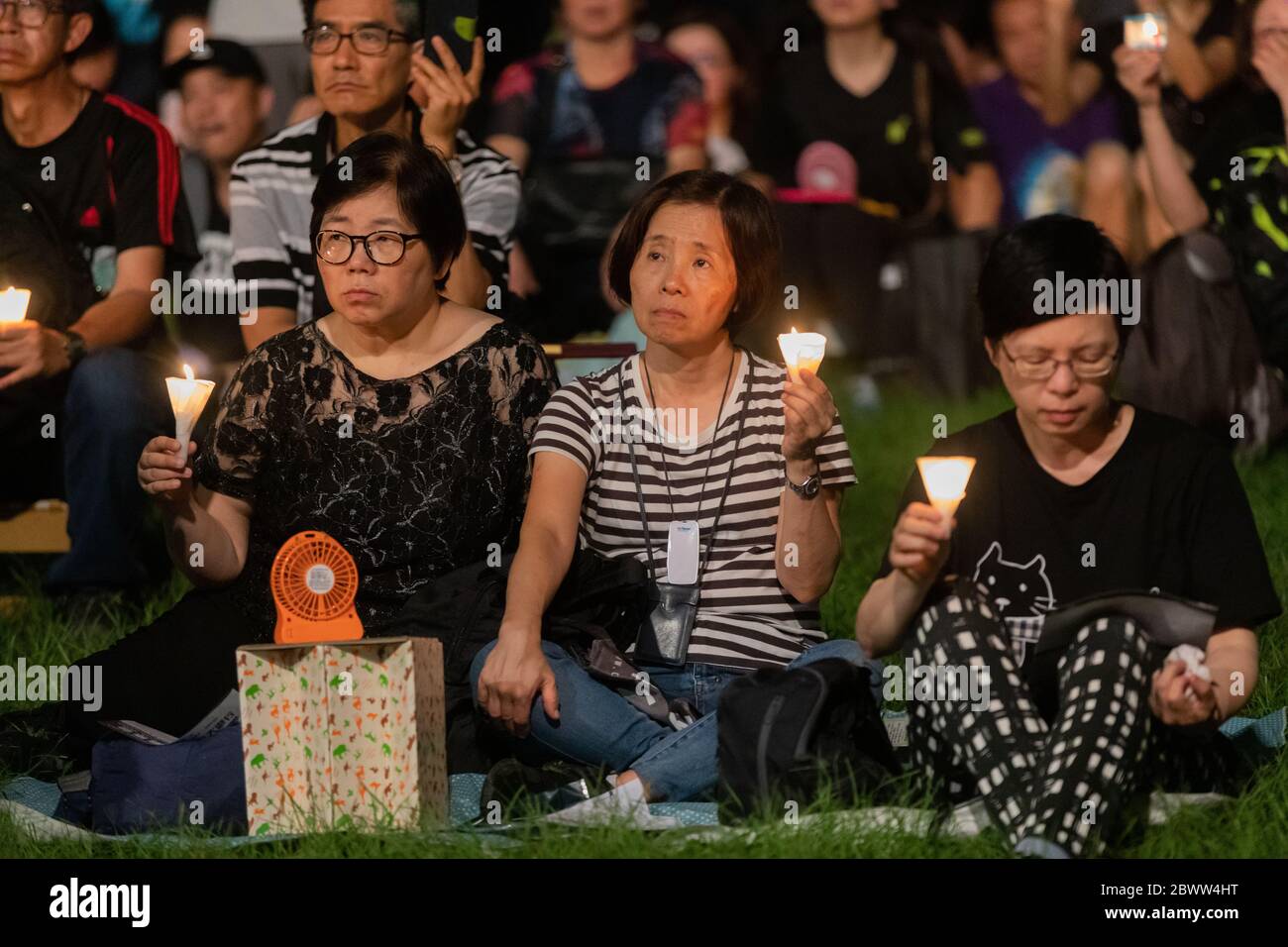 Los participantes de una Vigilia Masacre de la Plaza de Tiananmen en Hong Kong aparecen sombríos mientras escuchan los discursos en el escenario. 4 de junio de 2019 - Victoria Park, Hong Kong Foto de stock