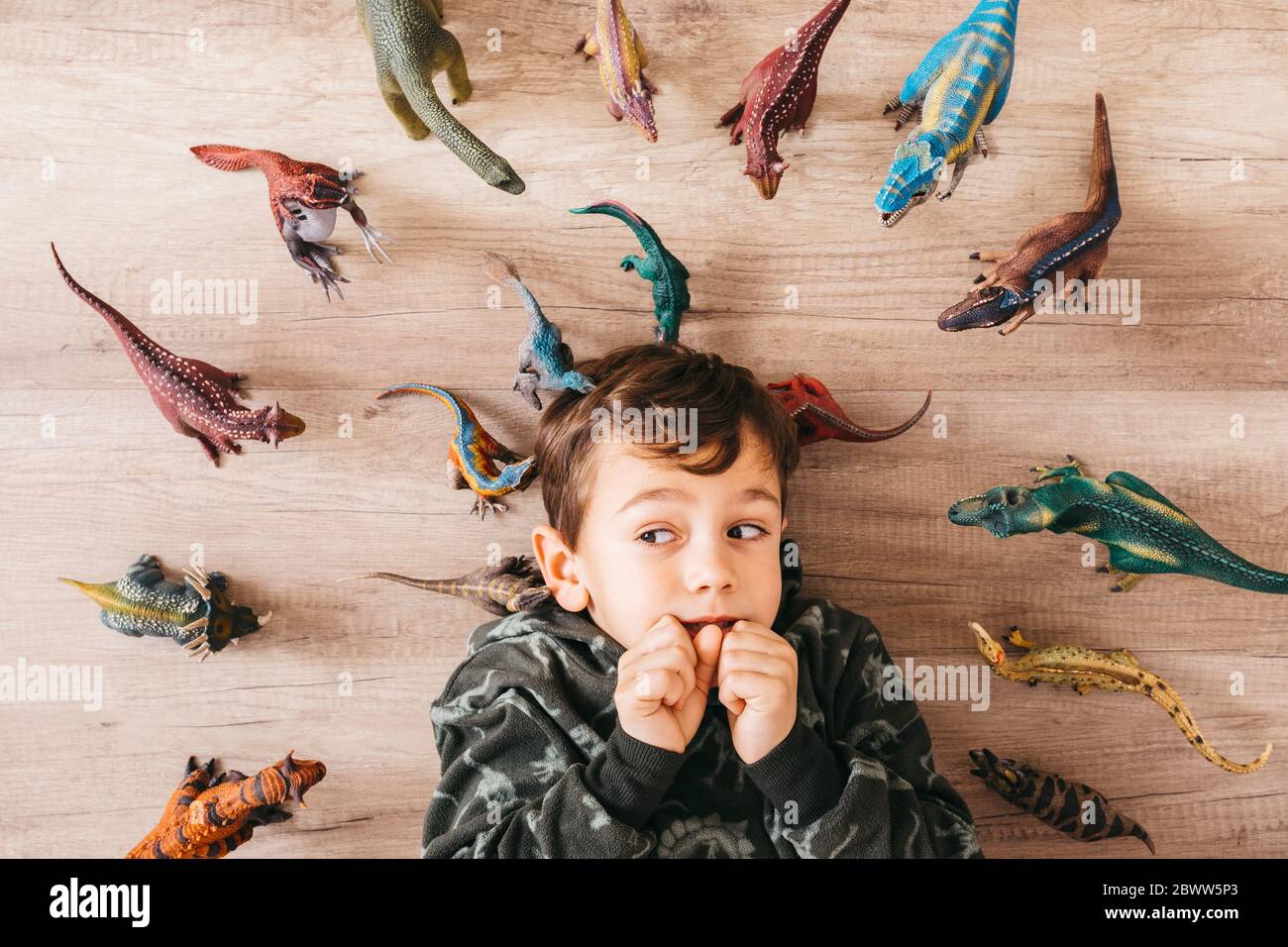 Retrato de un niño ansioso acostado en el suelo entre los dinosaurios de juguete Foto de stock
