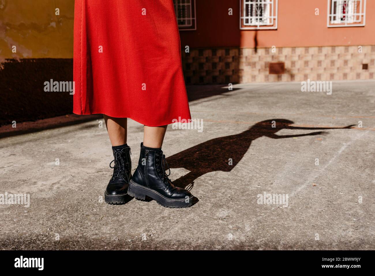 Mujer joven con vestido rojo y botas negras, jugando con su sombra en el  suelo Fotografía de stock - Alamy
