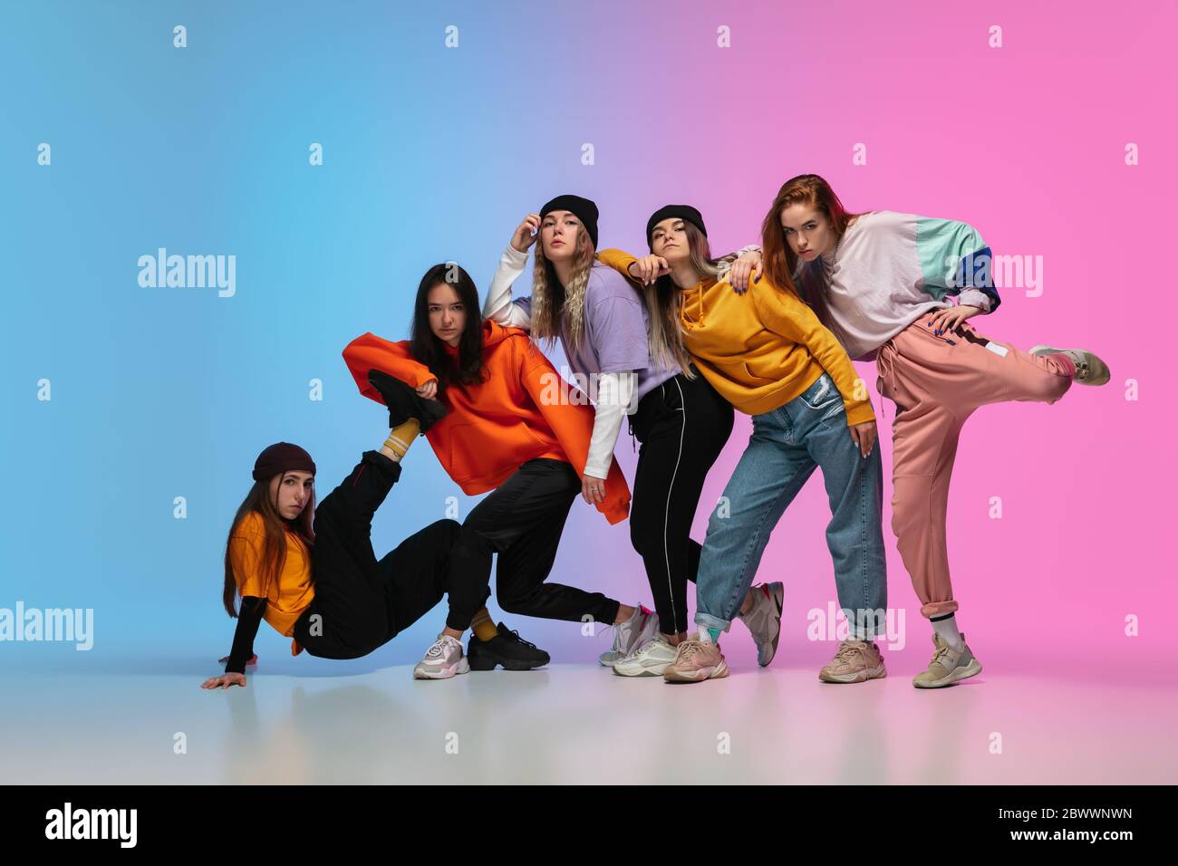 Grupo de bailarines, y niñas bailando hip-hop con ropa elegante sobre fondo de gradiente colorido en la sala de baile de neón. Cultura juvenil, movimiento, estilo y moda, acción. Retrato de