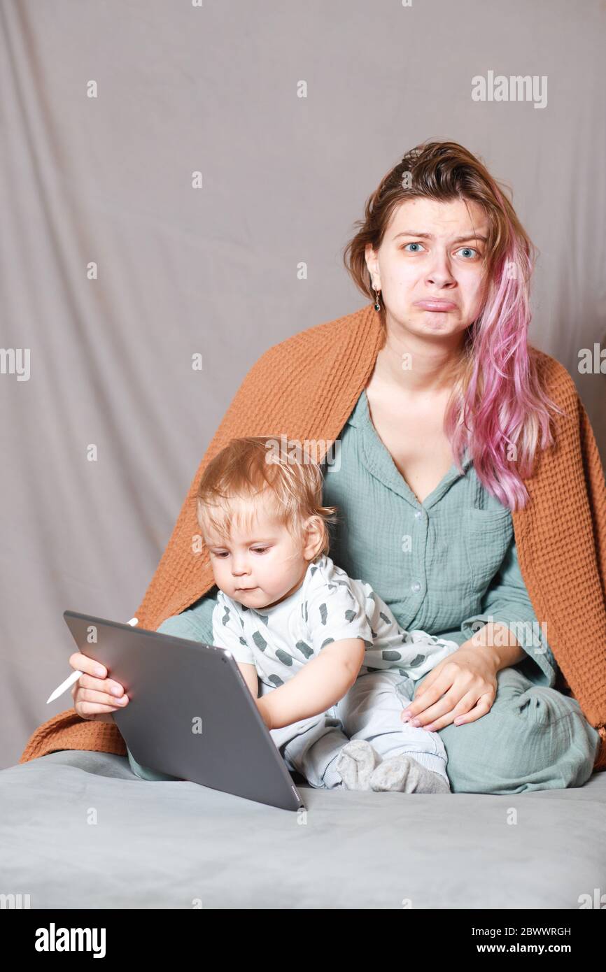 Una joven trabaja en casa con un ordenador de tableta, junto con un niño.el hijo quiere comunicarse con su madre, hacen ruido e interfieren ingenio Foto de stock
