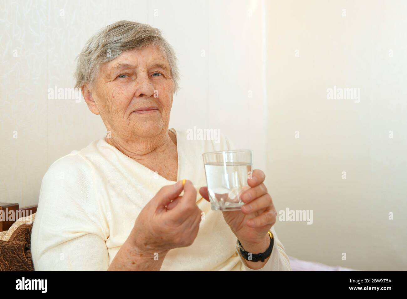 Una mujer anciana va a tragar un medicamento, una píldora y beberlo con agua. Foto de stock