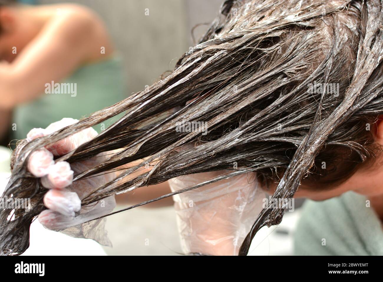 La joven tiñe su cabello en casa. La chica coloreando su cabello en su propio baño. Cuarentena, cuidado del cabello en casa, concepto de estancia en casa. Foto de stock