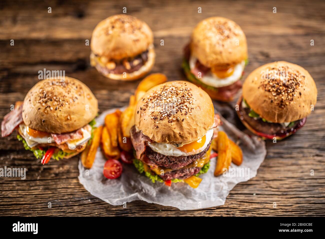 Selección de varias hamburguesas frescas sabrosas en bollos de sésamo con cuñas de patata en un ambiente rústico Foto de stock