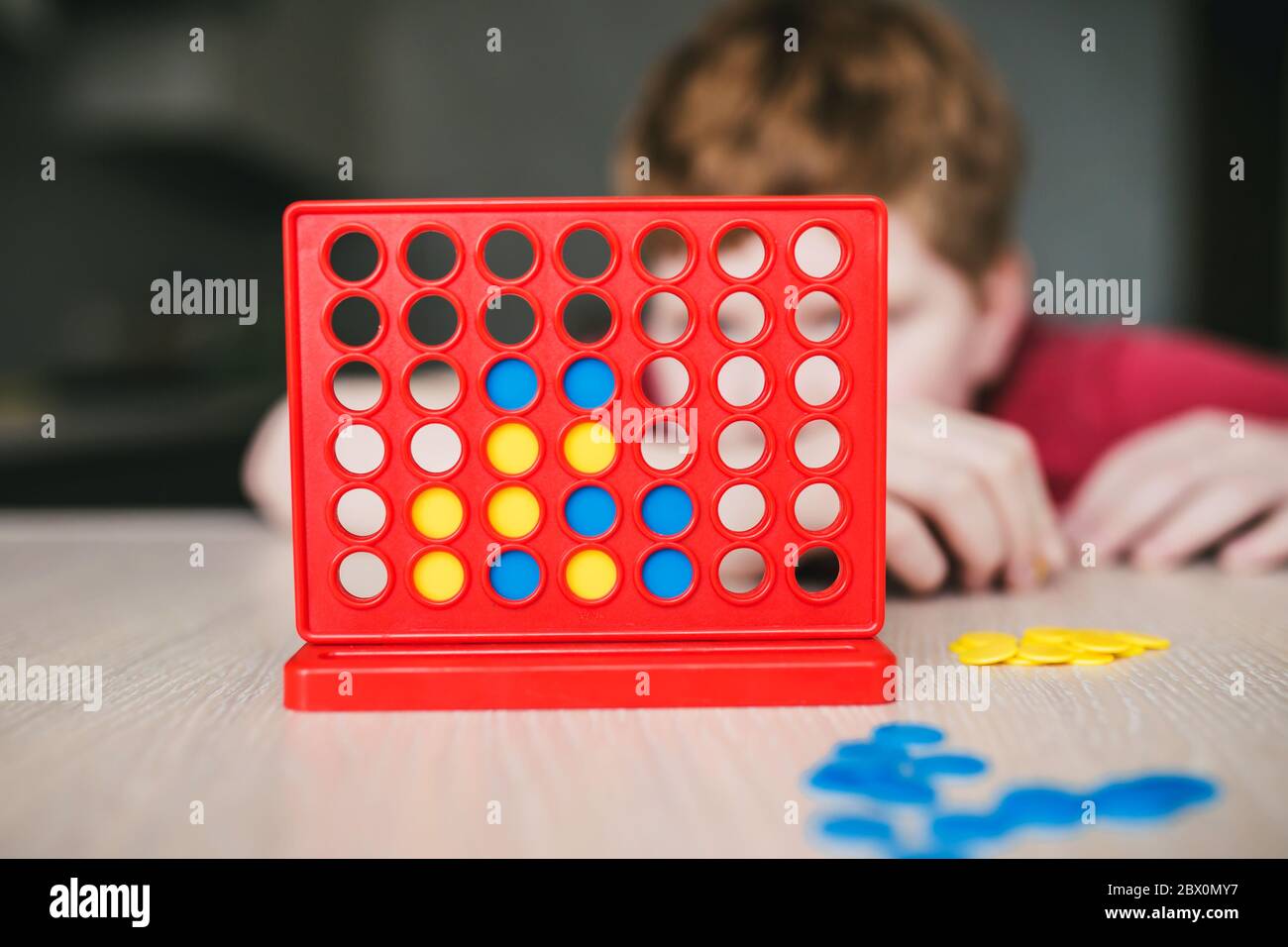 El chico se preguntaba jugar un juego de mesa cuatro en línea - el ocio en casa Foto de stock