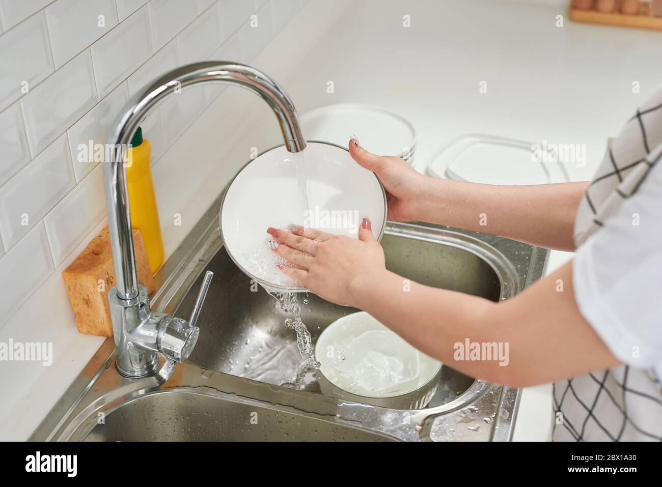 Mujer manos enjuagando platos bajo el agua corriente en el fregadero Foto de stock
