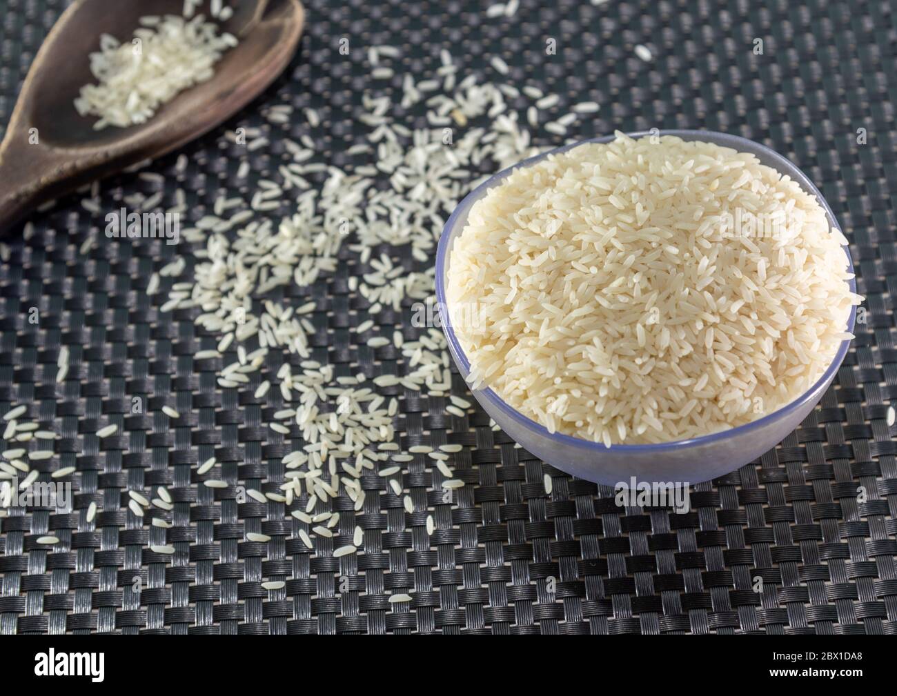 Arroz pelado y procesado de grano sobre fondo oscuro. Cereales de arroz y ornamentos de cocina. Granos semi-procesados en una olla de plástico y cucharas de madera. Foo Foto de stock