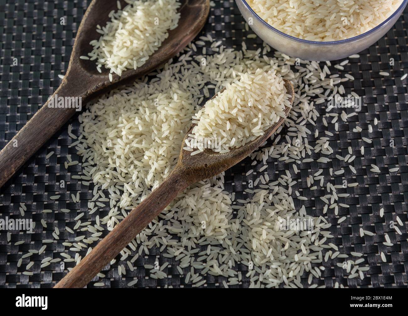 Arroz pelado y procesado de grano sobre fondo oscuro. Cereales de arroz y ornamentos de cocina. Granos semi-procesados en una olla de plástico y cucharas de madera. Foo Foto de stock