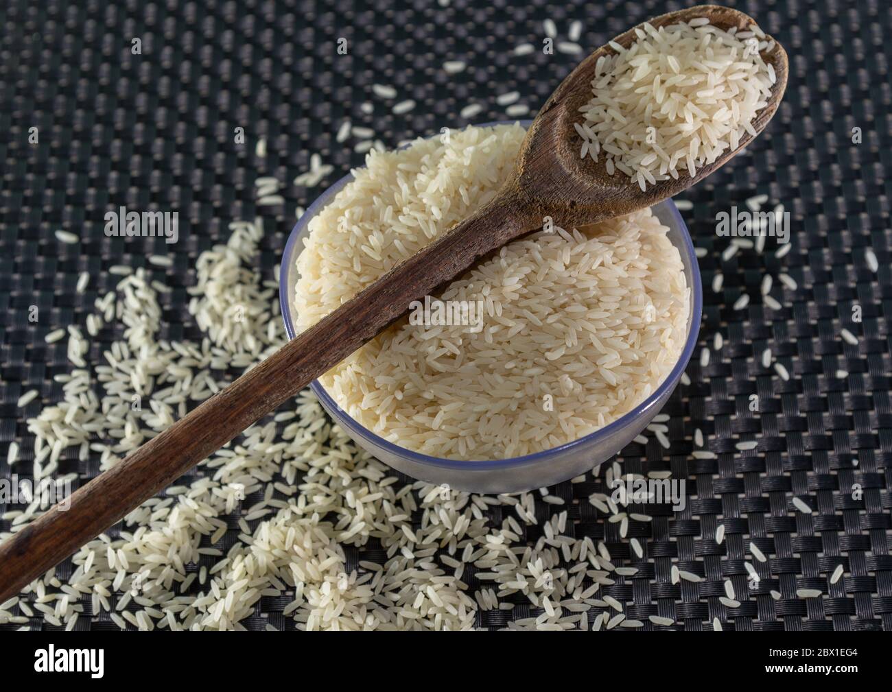 Arroz pelado y procesado de grano sobre fondo oscuro. Cereales de arroz y ornamentos de cocina. Granos semi-procesados en una olla de plástico y cucharas de madera. Foo Foto de stock