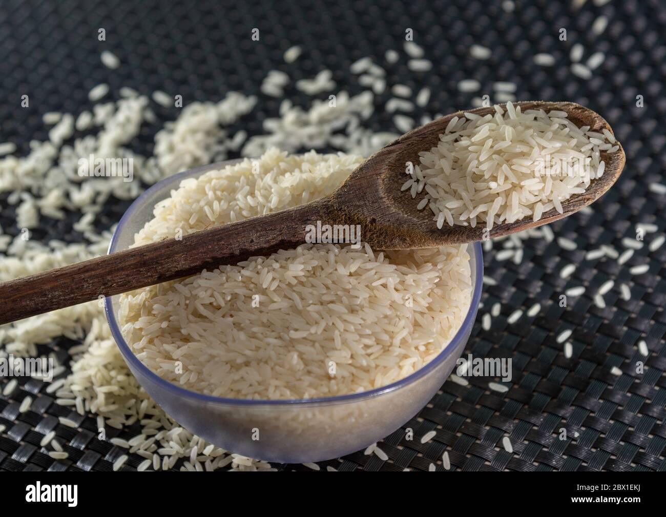 Arroz pelado y procesado de grano sobre fondo oscuro. Cereales de arroz y ornamentos de cocina. Granos semi-procesados en una olla de plástico y cucharas de madera. Foo Foto de stock