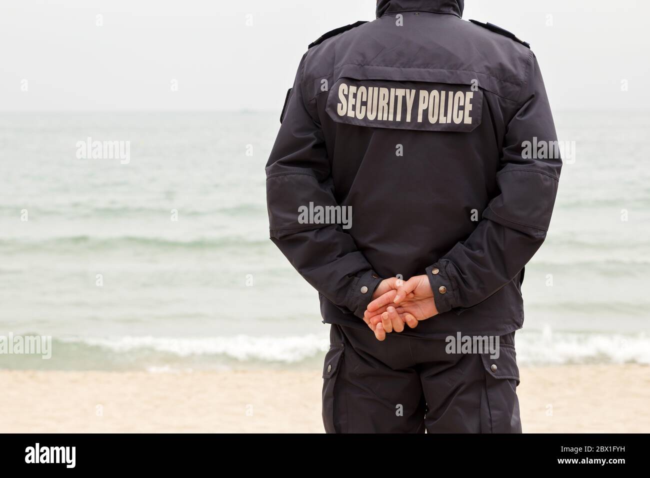Detrás de un hombre de la policía de seguridad con las manos apresadas custodiando en la costa Foto de stock