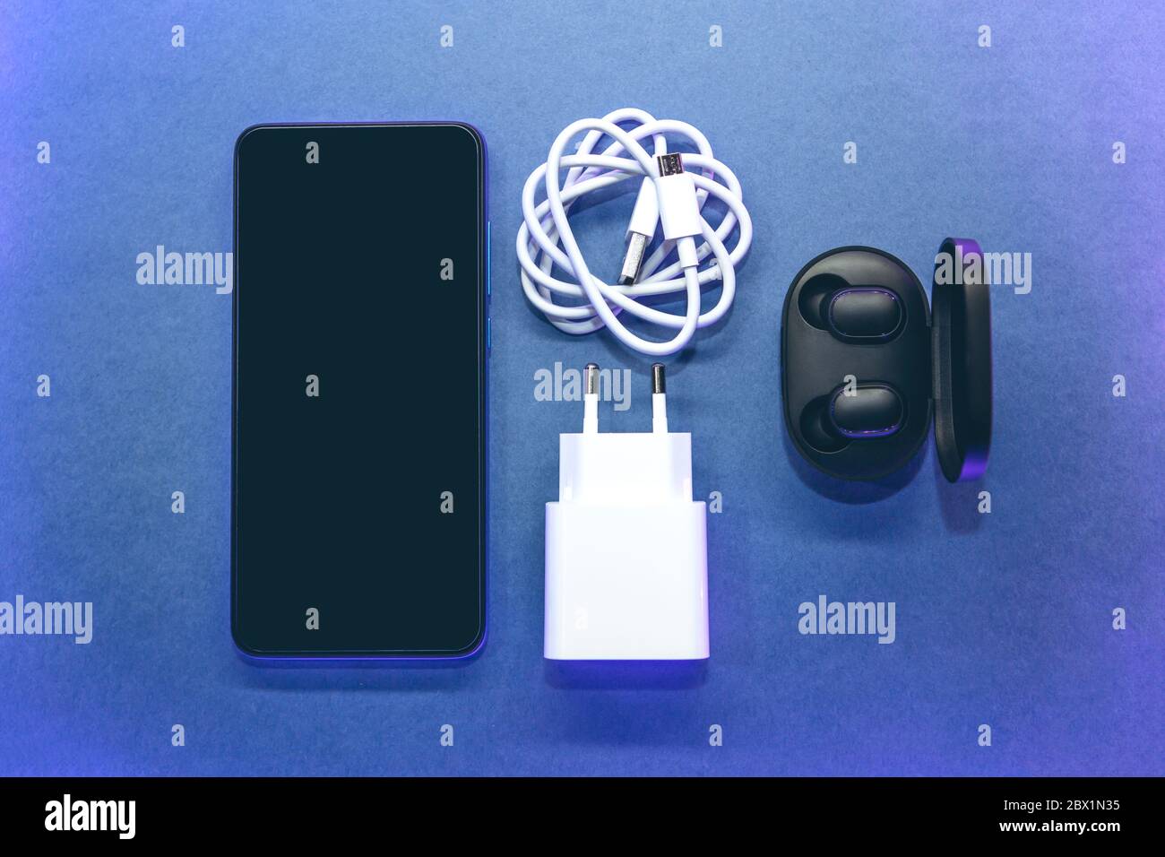 Juego de teléfono celular, auriculares inalámbricos y cargador sobre un  fondo azul Fotografía de stock - Alamy