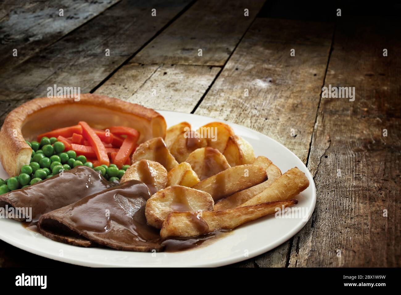 Cena tradicional asado los domingos con rosbif, pudín de yorkshire y verduras servidas en un plato sobre mesa de madera Foto de stock