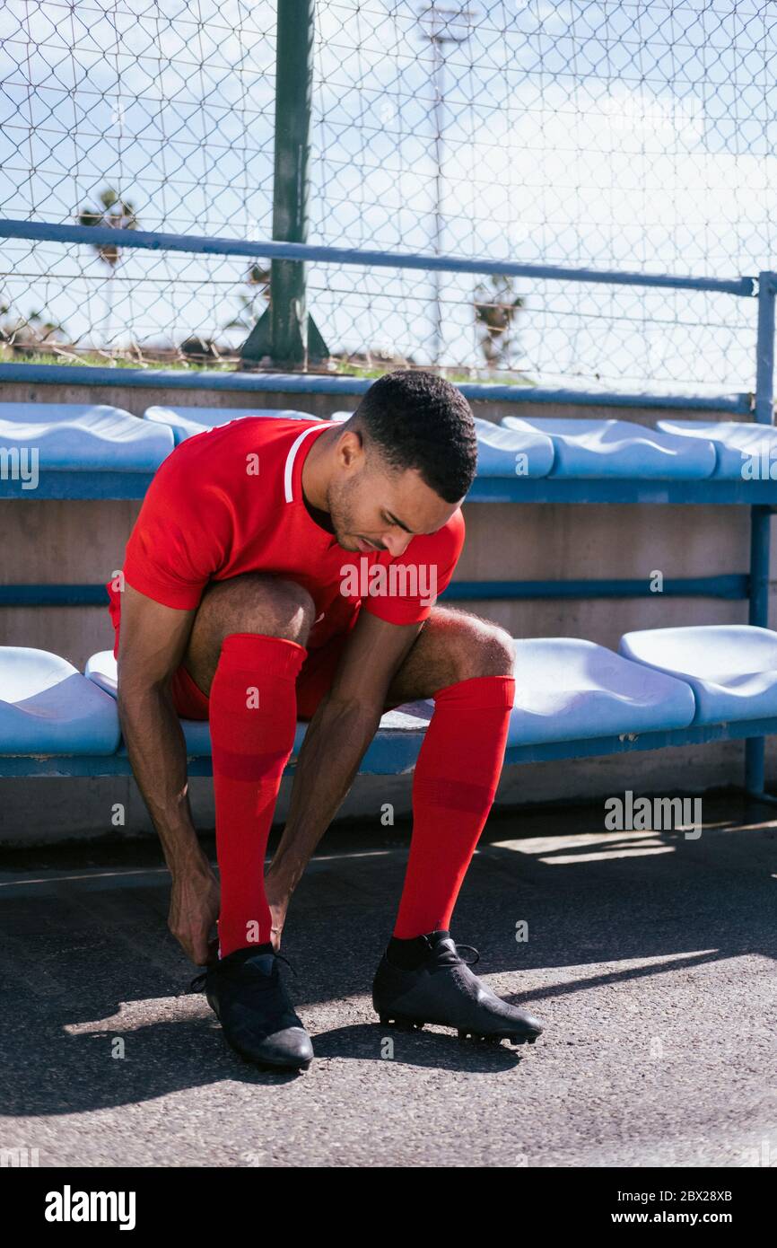 Jugador de fútbol americano africano sentado y fijando botas banco  Fotografía de stock - Alamy