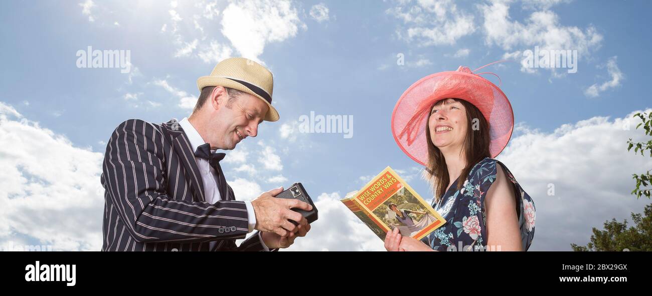 Bajo ángulo de primer plano de la feliz pareja británica en el traje vintage de los años 40 al aire libre en el sol de verano. El hombre está fotografiando a su esposa con la cámara clásica Box Brownie. Foto de stock