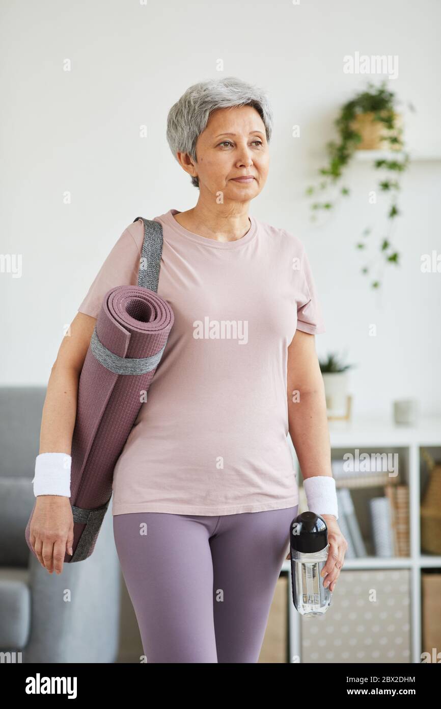 Mujer mayor en ropa deportiva y con colchoneta de ejercicio de pie